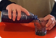 A woman pours a liquid from a bottle into a glass cup