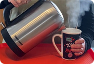 A woman pours a hot water from a kettle into a mug, steam is rising from the mug