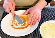 A woman is spreading margarine onto a piece of toast with a knife.