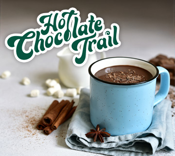 A blue cup filled with hot chocolate sitting on a folded towel with a white creamer cup