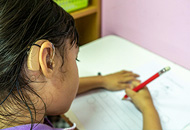 A girl wearing a hearing aid and sitting and writing in the classroom.