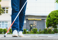 Person walking with a white cane in a cross walk in an urban setting