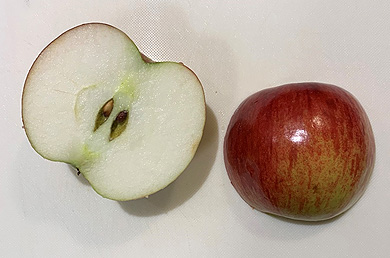 An apple cut in half on a white cutting board. One half of the apple faces down, showing the red peel and creating good contrast. The other half facing up showing the white flesh and poor contrast.