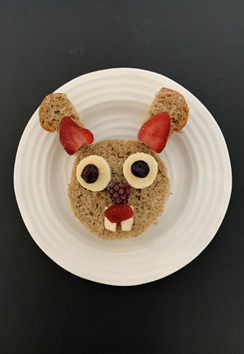 Bunny Sandwich 3 - Close up of bunny sandwich 2, made from circle cut bread, crusts with strawberries for ears, banana slices and blueberries for eyes, blackberry nose, strawberry mouth and rectangular cheese for teeth.
