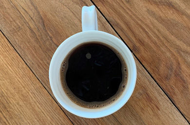 A white mug filled with coffee placed on a wooden brown surface.