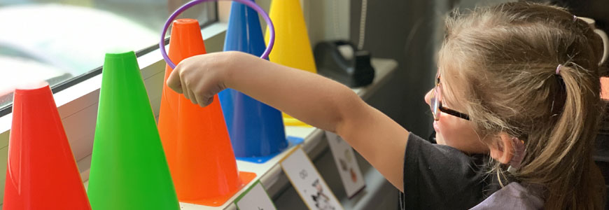 Student participating in a learning activity placing a small hoop over colorful cones