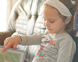 Blonde little girl with cochlear implant reading a book at home