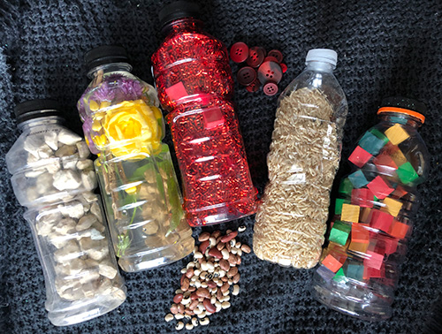 several bottles filled with various items. The contents include glitter &amp; sequins, small coloured wooden blocks, gravel and rice