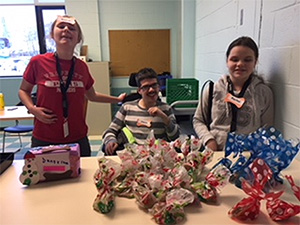 Three students stand behind a counter selling their packaged dog treats. A donation box sits to the left.