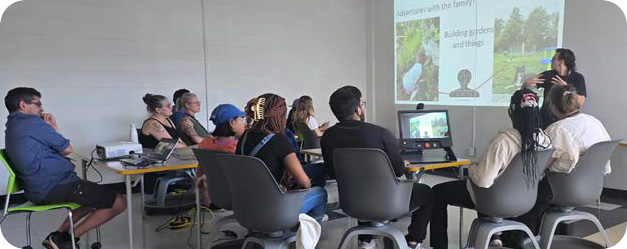 A group of high school students sit in a classroom-learning about DHH identity. A presentation is projected onto the wall showing images and text about family activities and building gardens.
