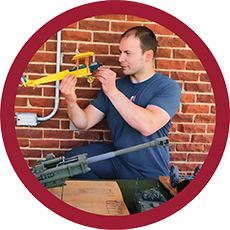 Aaron examining a small yellow model airplane while at a table with various military vehicle models in front of a brick wall.